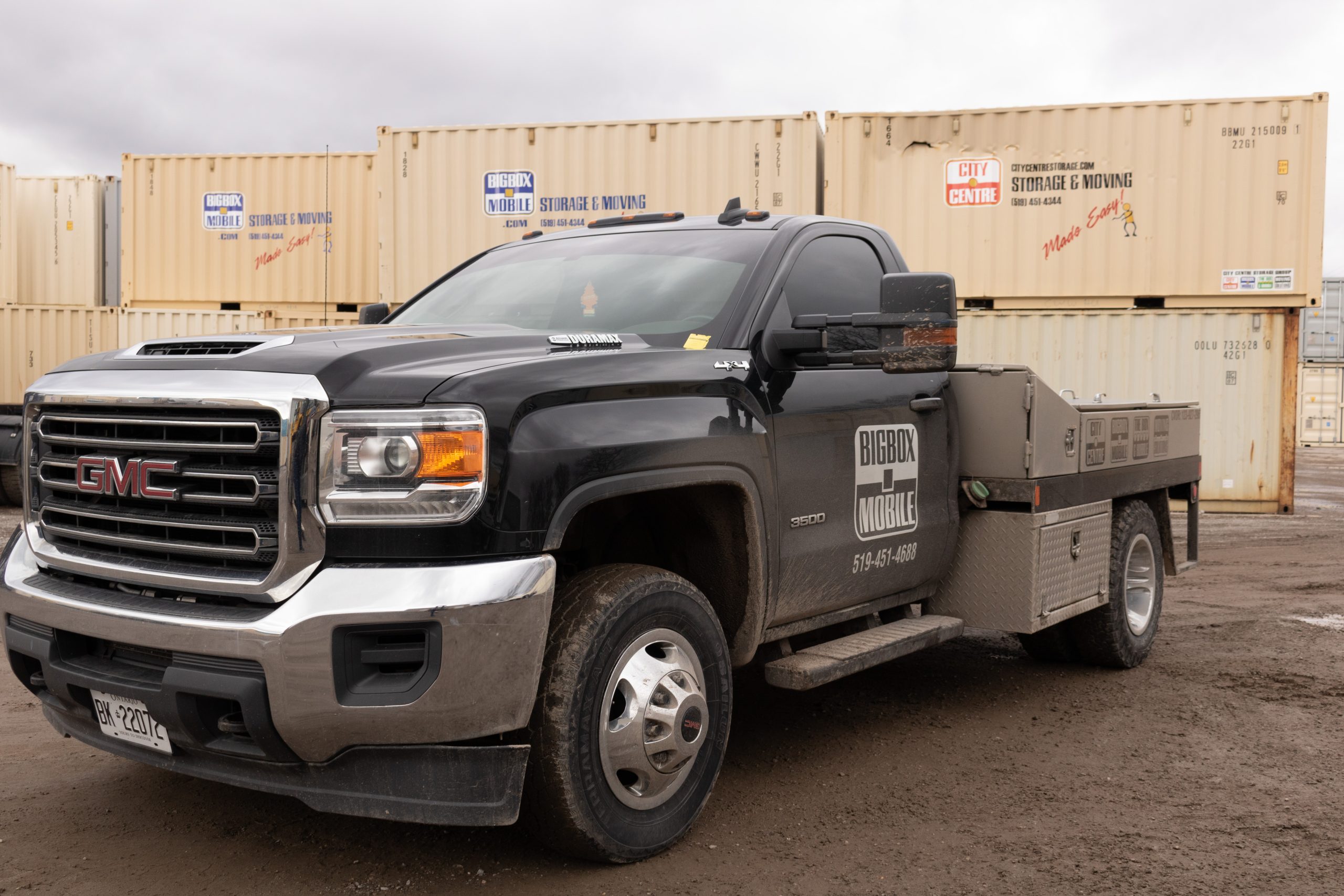 truck used to deliver mobile storage units in front of stacked shipping container storage bins