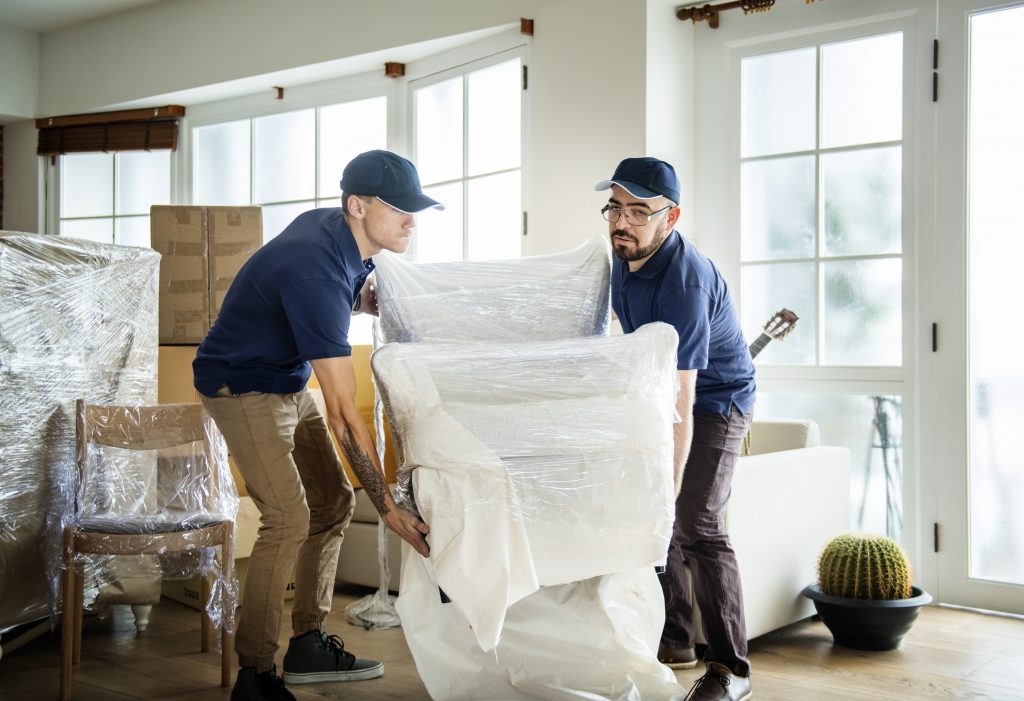 moving company employees lifting furniture in protective coverings